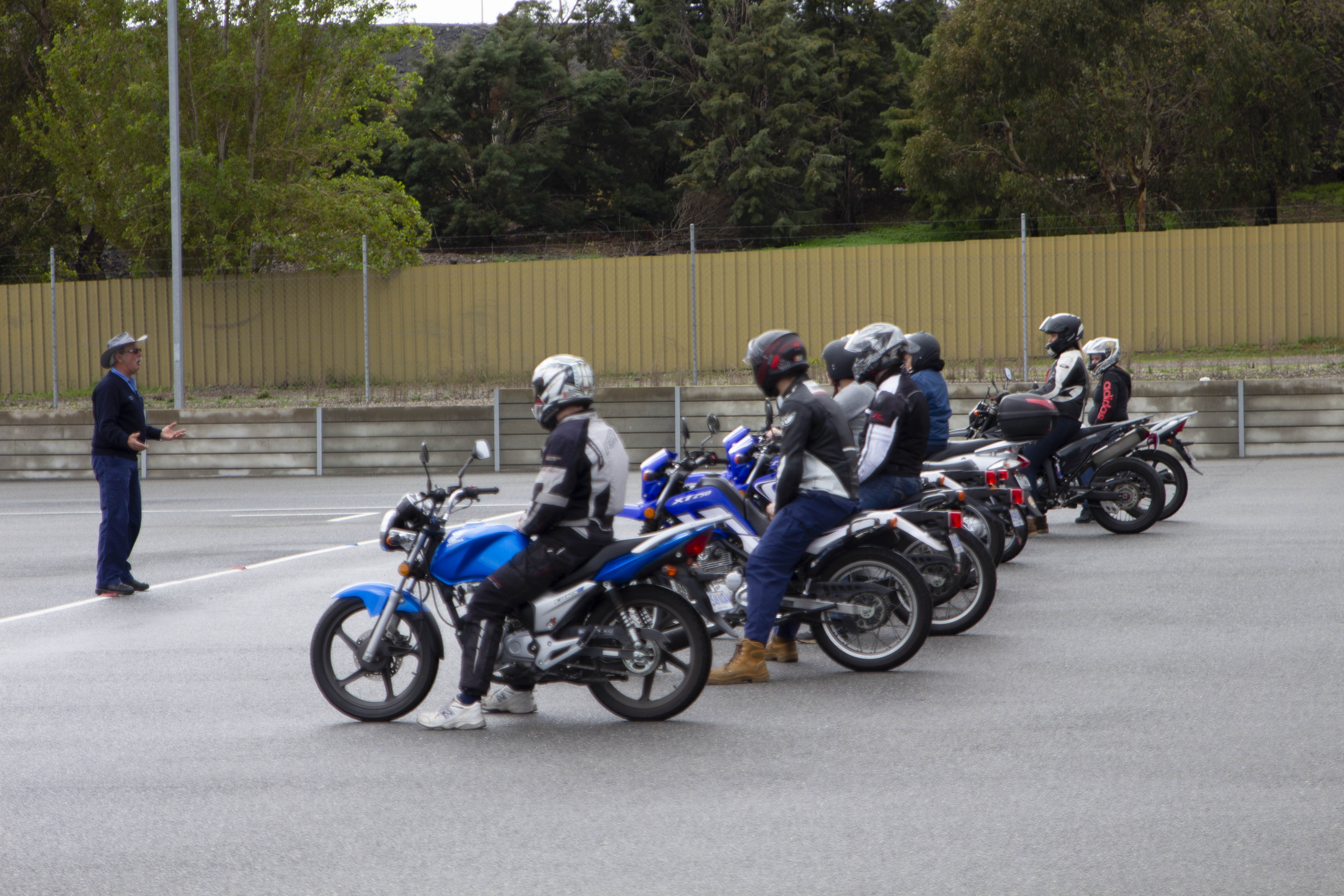 A group of motorcyclists, seated on their motorbikes, under instruction