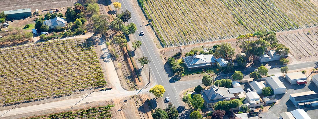 An aerial view of a regional road with vineyards and country homes on either side of the road